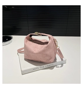 Detailed view of the pink suede shoulder bag with gold metal buckle on a white book