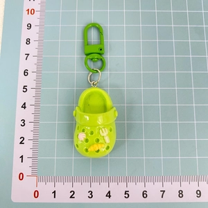 Close-up of a 4.5cm green clog shoe keychain with floral charms on a blue measuring mat