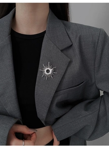 Close-up of a silver sunburst brooch with zircons on a dark grey suit lapel