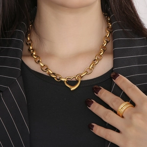 Close-up of a gold chunky heart necklace and double-row diamond ring on a model