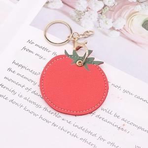Detailed view of a red faux leather tomato keychain with golden metal ring and green leaf