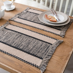 Woven cotton table runner with beige and black stripes and tassels on a wooden table