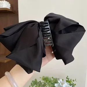 Detailed view of a large black satin bow hair claw clip held by hand for hair styling