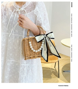 Detail of hand-woven rattan basket bag with pearl handle and silk ribbon accessory