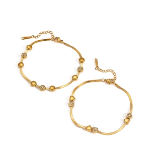 Détail de bracelets serpent dorés avec breloques cœur et perle en acier inoxydable