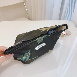 Detail of black butterfly jacquard cosmetic bag with smooth golden zipper and embroidery