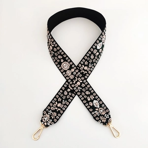 Close-up of thick floral embroidered bag strap with gold metal lobster clasps on white background