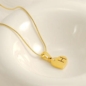 Collier coeur doré avec gravure H et diamant, présenté dans un bol en céramique blanche