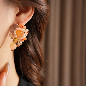 Elegant flower stud earrings featuring orange and clear crystals on a model's ear