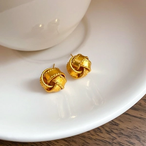 Detailed view of golden twisted knot stud earrings on a white ceramic surface