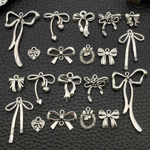Macro shot of 18 silver bow and heart charms for DIY jewelry making on black leather background
