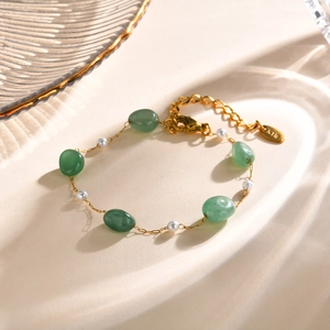 Detail of gold chain bracelet featuring green oval stones and white pearls with K18 tag