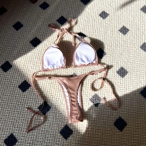 Flat lay of metallic rose gold bikini set with triangle cups on a textured rug
