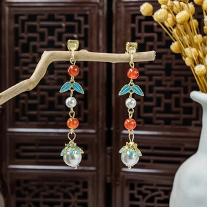 Detail of long tassel earrings with red beads and white pearl pendant on a wood branch