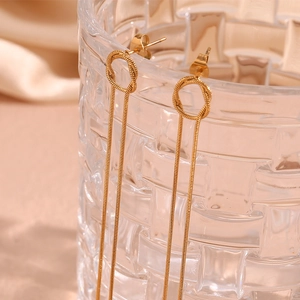 Macro shot of gold-plated woven snake chain tassel earrings on a textured glass rim