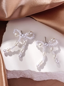 Detail of bow-shaped stud earrings with faux pearls on white stone and satin