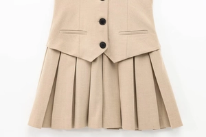 Dettaglio di abito a pieghe beige con bottoni neri e tasche decorative applicate