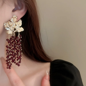 Detail of vintage gold leaf earrings with dark red grape cluster beads worn by model