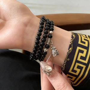 Gros plan du bracelet en perles noires avec breloque sac de chance argenté au poignet