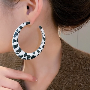 Macro view of large C-shaped cow print earrings on model for size perspective
