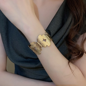 Detailed close-up of golden butterfly motif open cuff bracelet with metallic textures