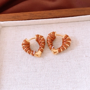 Close-up of 18k gold heart hoop earrings with brown leather wrap on a wooden tray