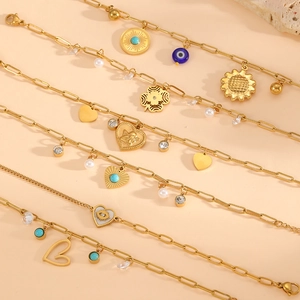 Close-up of gold chain bracelets set with evil eye, sun, and heart charms on stone base
