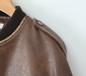 Détail macro de l'épaule d'une veste en cuir marron avec patte à bouton et col en maille