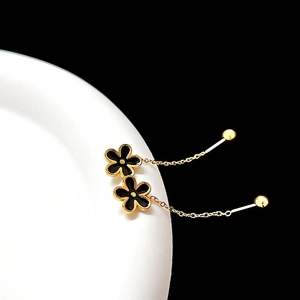 Detail of black enamel flower earring with gold chain and bead on white ceramic tray