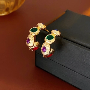 Macro shot of vintage gold C-shaped earrings with colorful gemstones and hammered texture