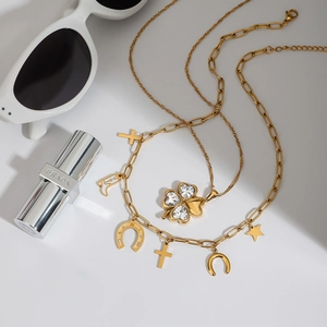 Detail of gold necklace with clover cross and star charms on white background