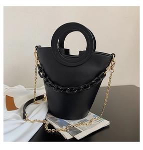 Detail of black bucket bag with a round handle, thick chain, and matte leather texture