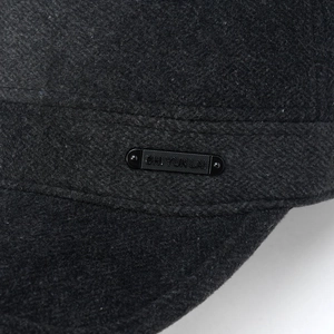 Macro detail of dark grey wool blend fabric and metallic logo on the flat top winter cap
