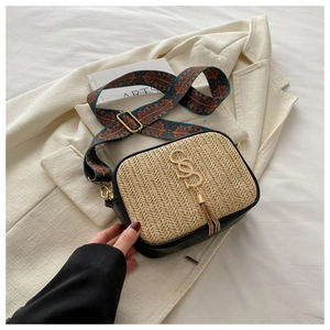 Detail of woven straw handbag with black leather trim, gold SDS logo, and fabric strap