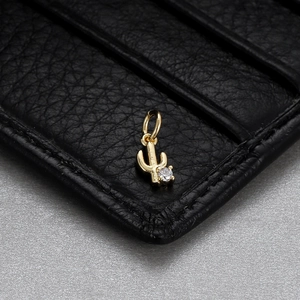 Macro shot of a golden cactus pendant charm with a tiny crystal on black leather texture
