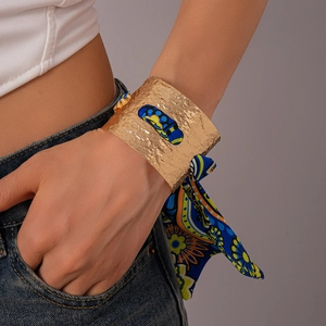 Dettaglio di un bracciale rigido dorato martellato con foulard in seta a stampa blu