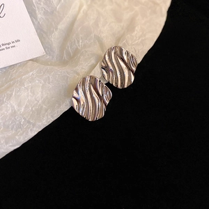 Close-up of irregular silver stud earrings with liquid wavy metal texture on black background