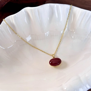 Macro shot of polished red oval pendant with golden chain on white shell tray