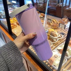Close-up of hand holding a 30oz purple gradient tumbler with white carry lid in a cafe