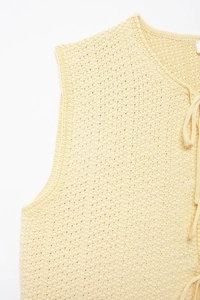 Detail of light yellow knit vest showing hollow crochet texture and V-neck tie closure
