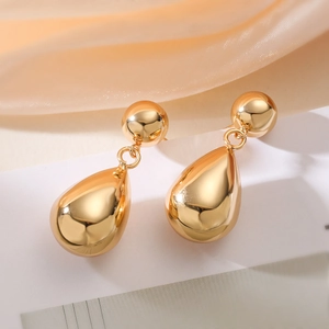 Close-up of polished gold double teardrop earrings on elegant peach silk background