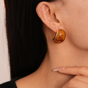 Detail of amber resin earring with gold metal trim shown on model's ear in close-up