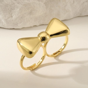 Exaggerated golden double-ring bow jewelry on a beige surface with soft lighting