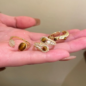 Detailed view of zircon tiger eye rings in brass gold plating on hand with warm lighting