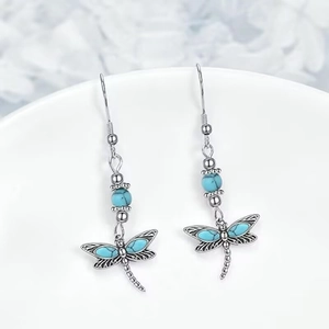Bohemian silver dragonfly drop earrings featuring turquoise beads on a white ceramic rim