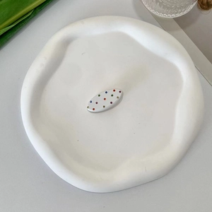 Detail view of a white oval hair claw clip with colorful polka dots on a minimalist plate