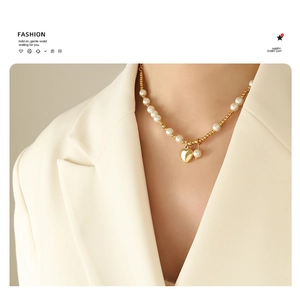 Detail view of a gold heart pendant necklace with pearls on a model wearing a blazer