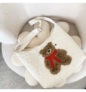Close-up of a white quilted tote bag featuring a cute brown teddy bear plush patch detail