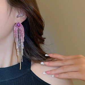 Close-up of model wearing long gradient pink rhinestone fringe earrings on warm background