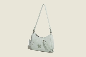 Close-up of pale green textured shoulder bag featuring butterfly applique and silver hardware